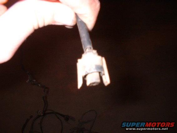 Hand holding a white electrical connector with a black wire attached. Loose wires are visible below