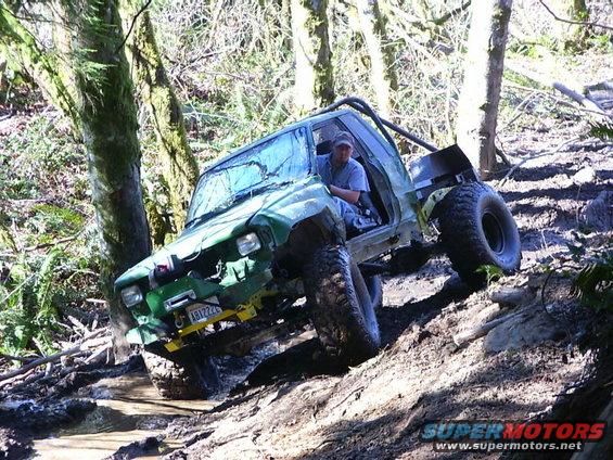 Green off-road vehicle with roll cage stuck in mud on a steep incline, driver visible inside