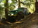 1990 Ford Bronco - This heavily modified off-road vehicle navigates a challenging wooded terrain with a visible roll cage.