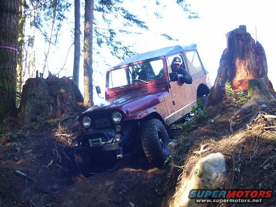 Red Jeep CJ-7 navigating a difficult off-road trail with large tree stumps and rocks