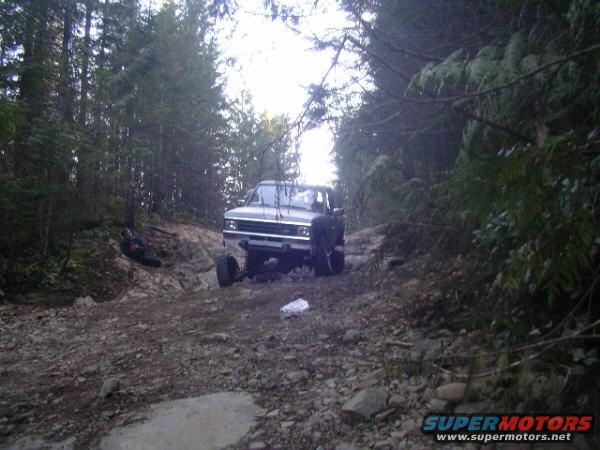 Truck on a rocky, wooded trail. It looks like a Ford Bronco II, but the body style is more like a Ford Ranger or similar compact pickup from the mid-80s