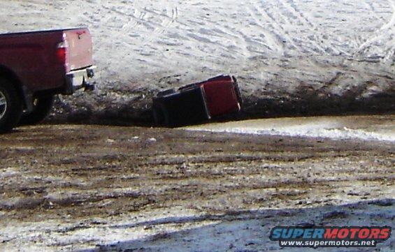 Red pickup truck overturned in a snowy ditch next to another red pickup truck