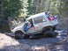 1990 Ford Bronco - This heavily modified off-road vehicle is navigating a challenging muddy terrain in a wooded area.