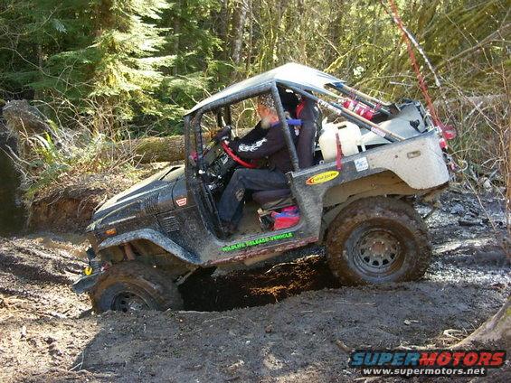 Black off-road vehicle with roll cage stuck in mud, driver visible