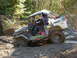 1990 Ford Bronco - An off-road vehicle navigates a muddy trail through a forest.