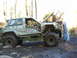 1990 Ford Bronco - Two people work on a heavily modified off-road SUV stuck in the mud on a trail.