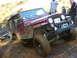 1990 Ford Bronco - A maroon Jeep CJ-7 is stuck in the mud off-road, with several people observing the situation.