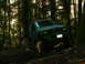 1990 Ford Bronco - A green off-road vehicle navigates a challenging trail through a dense forest.