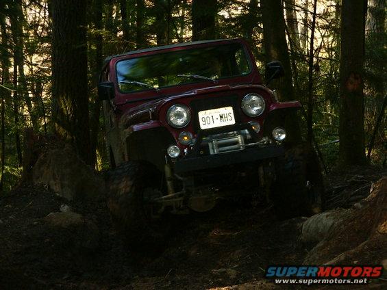 Red Jeep CJ-7 off-roading on a muddy trail with trees