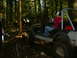 1990 Ford Bronco - Multiple Jeeps navigate a muddy, wooded trail with dense trees and uneven terrain.
