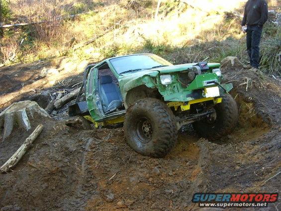Modified off-road vehicle with large tires stuck in mud, front end damaged