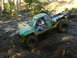 1990 Ford Bronco - A modified green truck navigates a challenging muddy terrain, with its tires deep in the mire.