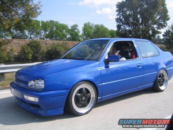 Blue coupe with black rims driving on a road