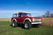 1975 Ford Bronco - A red and white 1975 Ford Bronco is shown from a three-quarter front view, parked in a grassy field under a clear blue sky.