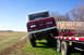 1975 Ford Bronco - A red 1975 Ford Bronco is loaded onto a trailer, with another red truck visible in the background.