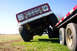 1975 Ford Bronco - A red 1975 Ford Bronco is positioned on a trailer, with its front grille and suspension clearly visible against a bright blue sky.