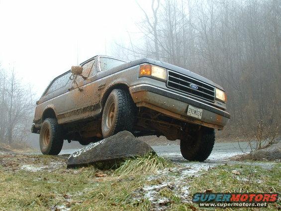 Mud-covered Ford Bronco, 1987 model year, driving off-road on a rock