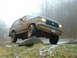 1991 Ford Bronco - A muddy 1987 Ford Bronco navigates an off-road obstacle on a foggy day.