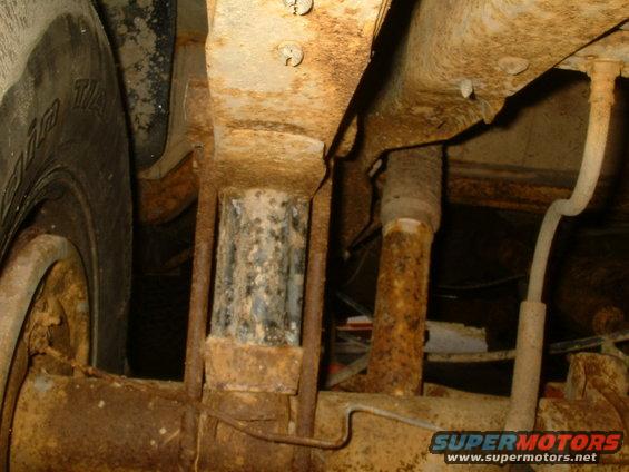 Undercarriage of a rusty vehicle showing suspension components and a tire