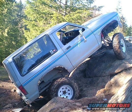 Silver 1983 Ford Bronco II off-roading on rocks, angled to the right, with lifted suspension and large tires