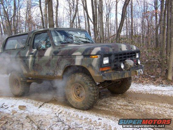 Camouflage 1979 Ford Bronco driving off-road, kicking up dust
