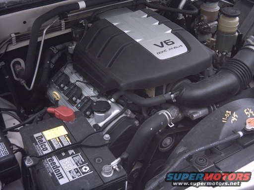 engine bay with V6 DOHC engine cover, Delco battery, and hoses