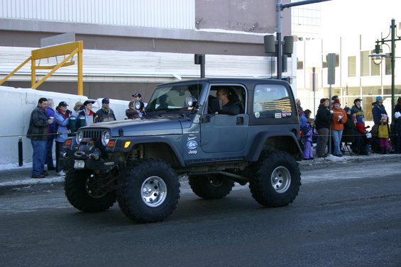Dark blue 2003 Jeep Wrangler with winch and large tires driving in a parade