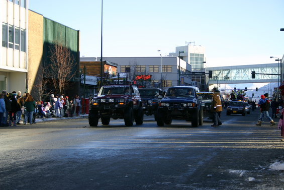 Red Jeep TJ with lifted suspension and off-road tires, seen from a 3/4 front angle during a parade