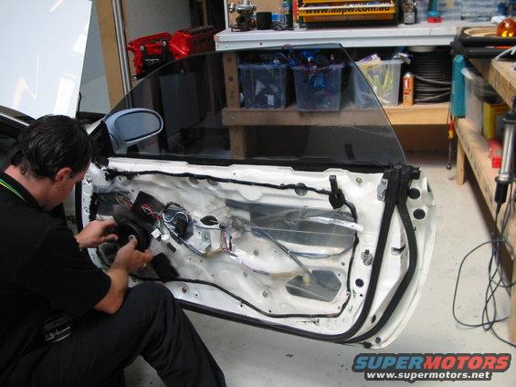 Man working on the inside of a car door, installing a speaker. Wires and door mechanisms are visible