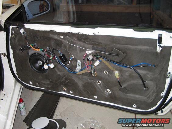 Car door panel removed, showing speaker and exposed wiring harness. A can of spray is on the floor