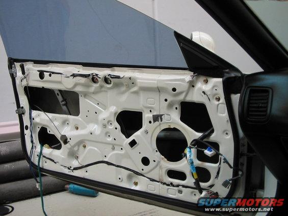 Car door with interior panel removed, showing wiring and internal structure. A blue object is on the floor