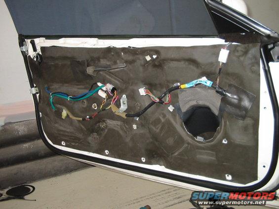 Car door interior panel removed, showing wiring harness and sound dampening material. White exterior paint visible