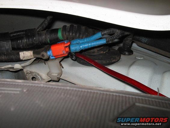 Close-up of automotive wiring harness with blue tape on connectors and a red wire