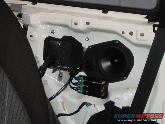 Car door interior showing speaker, black plastic housing, and wiring harness with green connector block