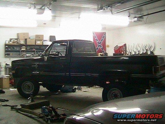 Black pickup truck, side view, in a garage with tools and a Confederate flag