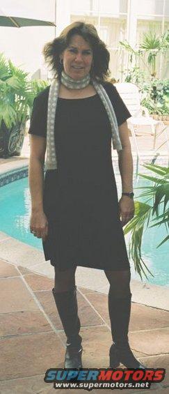 Woman in black dress and boots standing by a swimming pool with palm trees