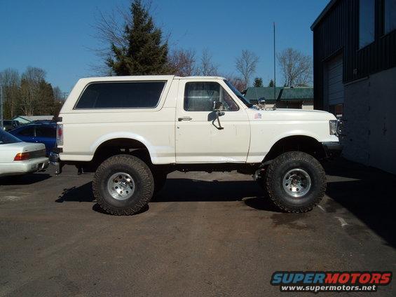 White 1989 Ford Bronco lifted with large tires, parked outside a building