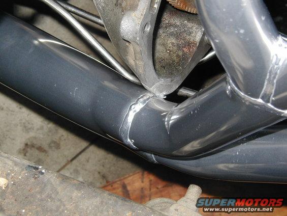 Gray exhaust headers with visible welds, attached to engine block