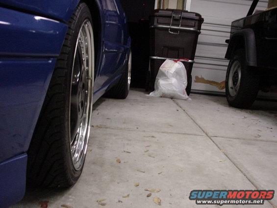 Blue sedan's rear wheel and side panel, next to a black Jeep in a garage