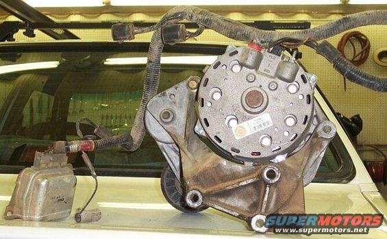 Alternator and voltage regulator assembly on a white surface, with wiring harness