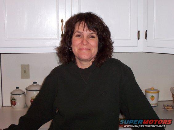 Woman in a dark sweater stands in a kitchen with white cabinets and countertop