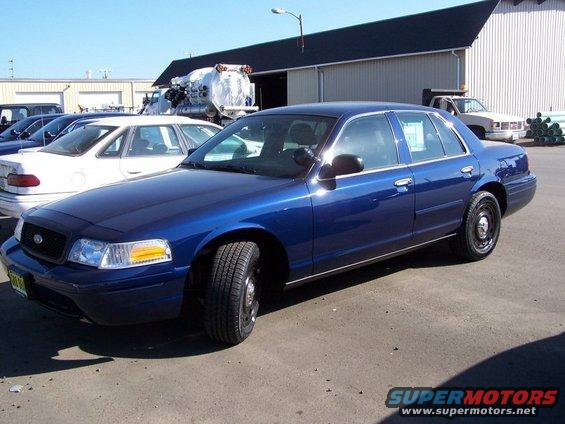 Blue 2001 Ford Crown Victoria parked outside with a white car and a truck in the background
