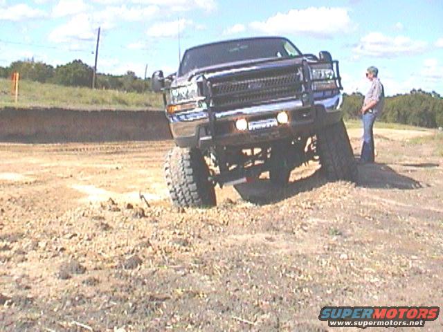 Dark blue Ford F-Series truck with a brush guard, lifted suspension, and large tires on a dirt mound