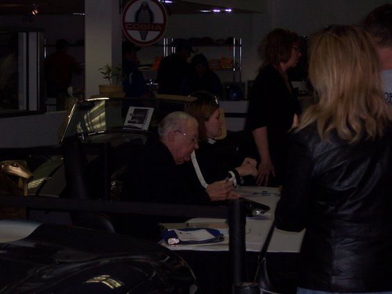 People signing autographs at a table with a Cobra logo in the background