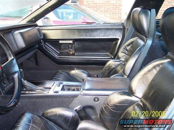 Black leather car interior with cracked seats, dashboard, and center console. Another car is visible through the window