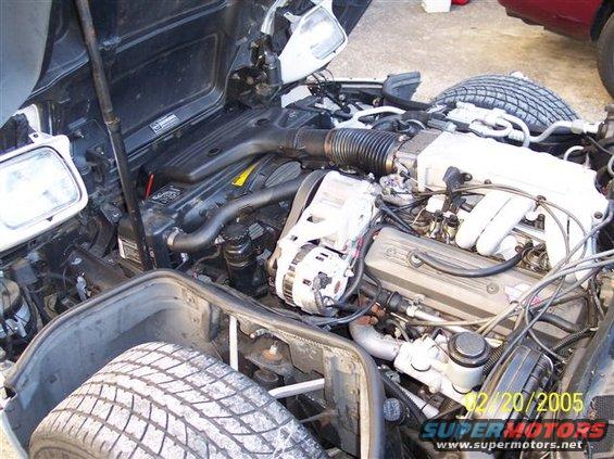 Engine bay of a car with a spare tire visible in the front left fender well. Date stamp reads 12/20/2005