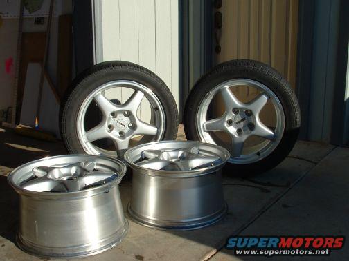 Four aftermarket alloy wheels with tires, two standing and two lying down