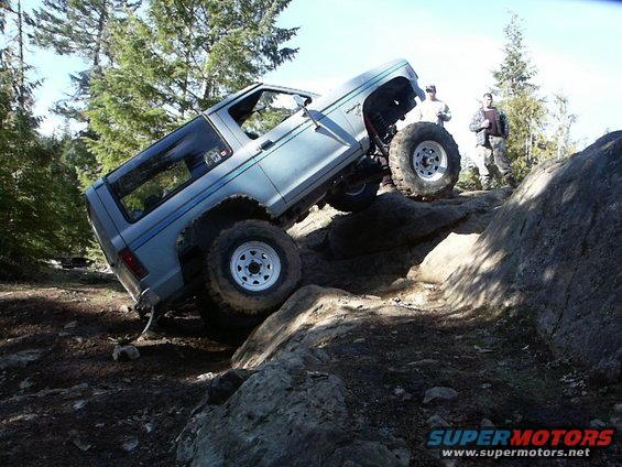 Light blue SUV with off-road tires climbing over large rocks