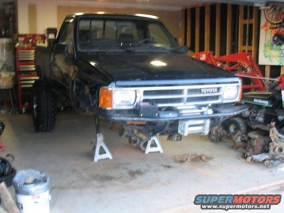 Black Toyota pickup truck with front end removed, sitting on jack stands in a garage