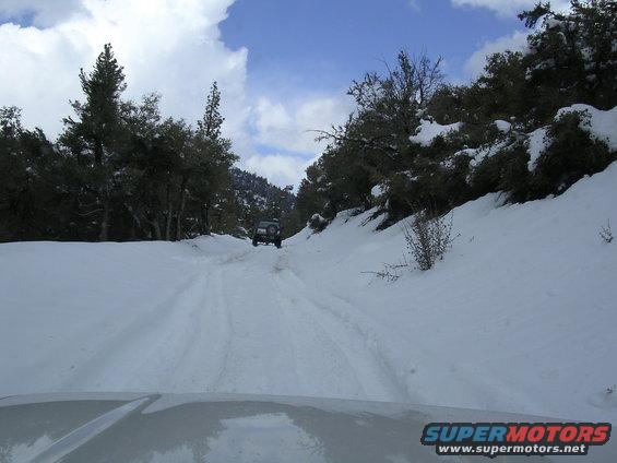 SUV driving on a snow-covered road with trees and snow on the sides